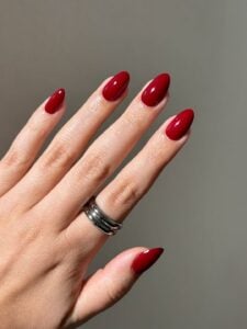 Mão de pele clara, com anel prata e unha amendoada vermelho-cereja