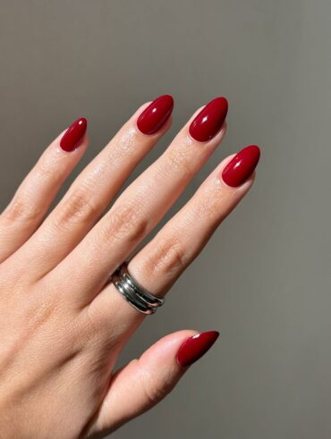 Mão de pele clara, com anel prata e unha amendoada vermelho-cereja