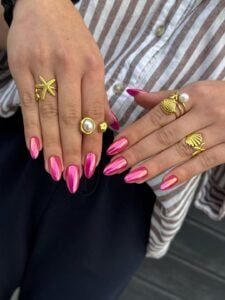 Mãos de pele clara, com anéis em dourado e unha amendoada rosa croamada