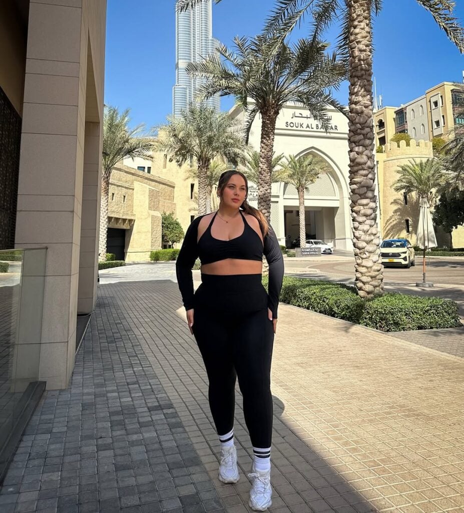 Mulher jovem, de pele clara e plus size. Ela usa top, manguito, calça legging, meias brancas e tênis branco