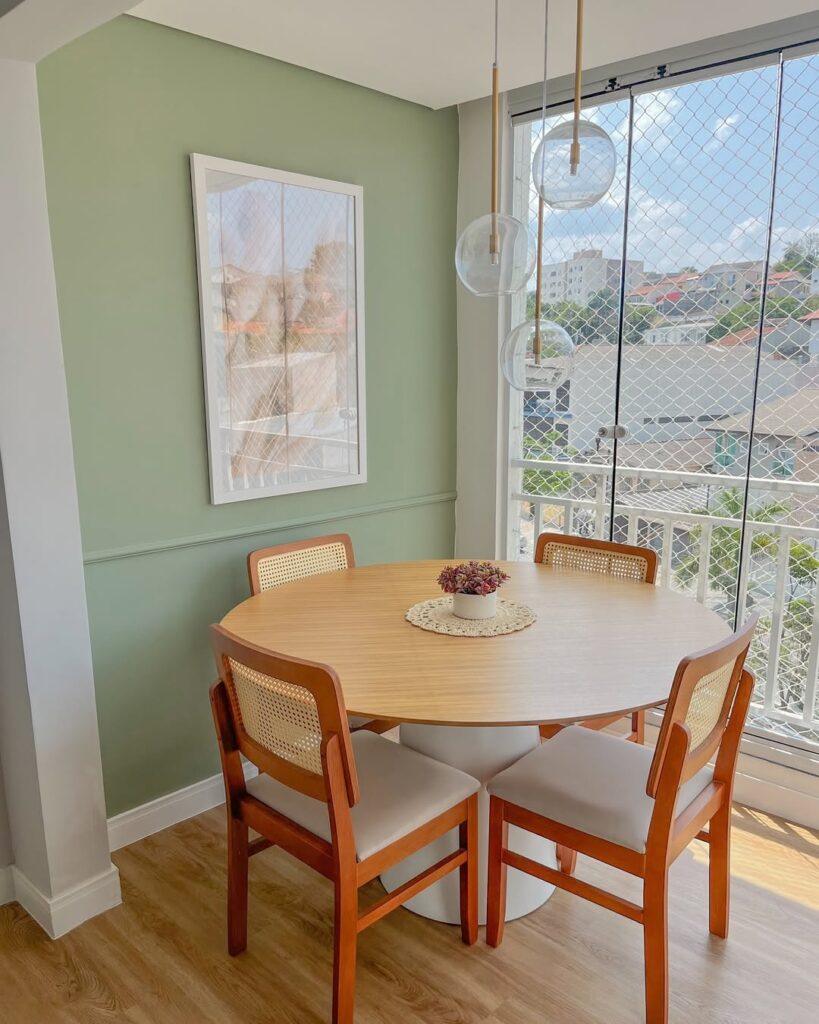 Varanda com mesa redonda e cadeiras com assento claro e parede verde-clara com quadro
