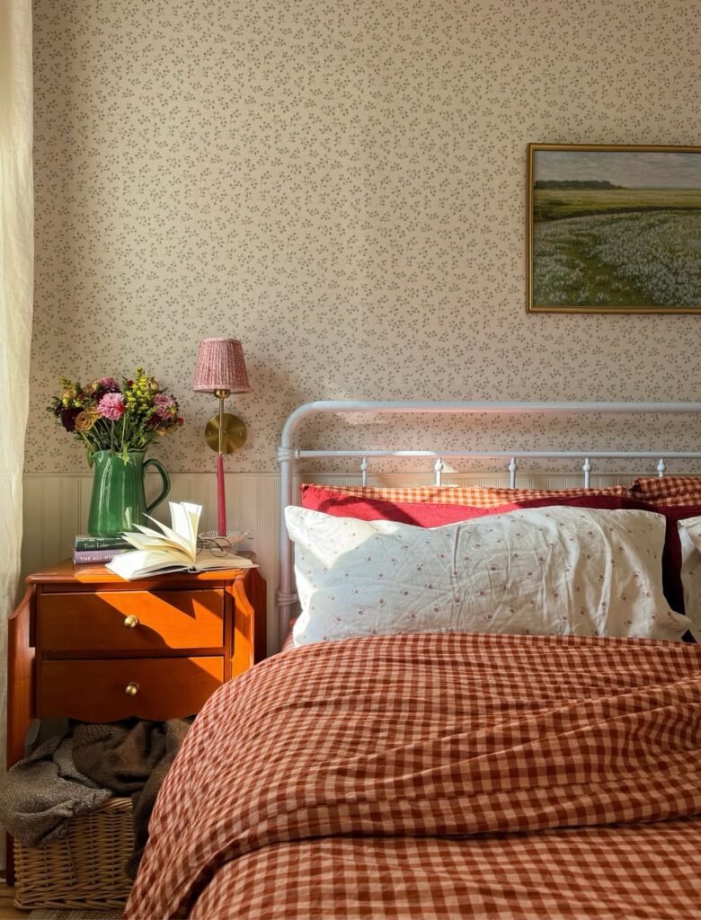 Quarto com papel de parede delicado, mesa de cabeceira de madeira com vaso e flores, livros e luminária