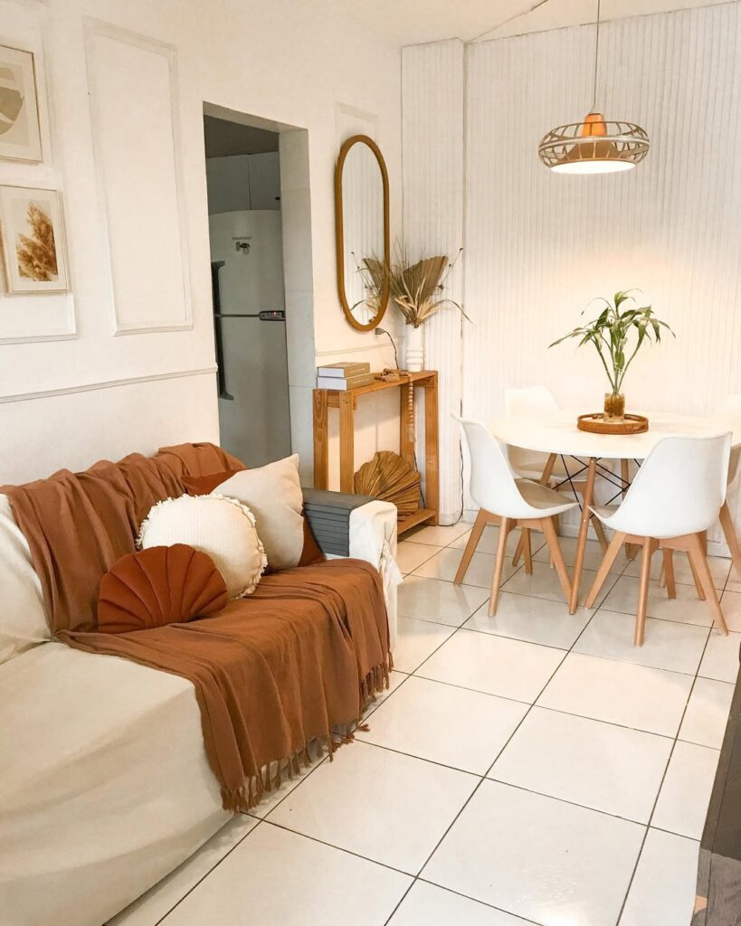 Sala de estar e jantar integradas, sofá com manta e almofadas, mesa redonda com cadeiras e pendente acima
