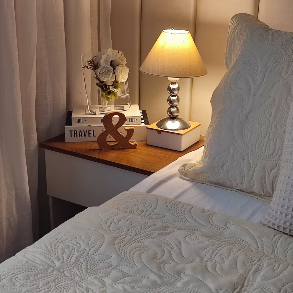 Mesa de cabeceira com livros decorativos, abajur com design diferente e vaso com flores
