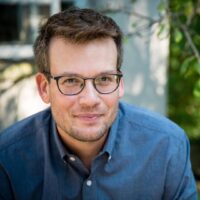 John Green com camisa azul e óculos preto