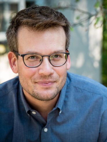 John Green com camisa azul e óculos preto