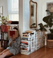 Mulher de pele clara sentada, lendo, com livros atrás
