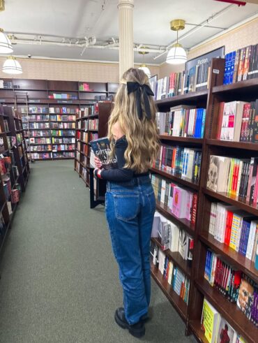 Mulher de pele clara, com cabelo loiro em uma biblioteca