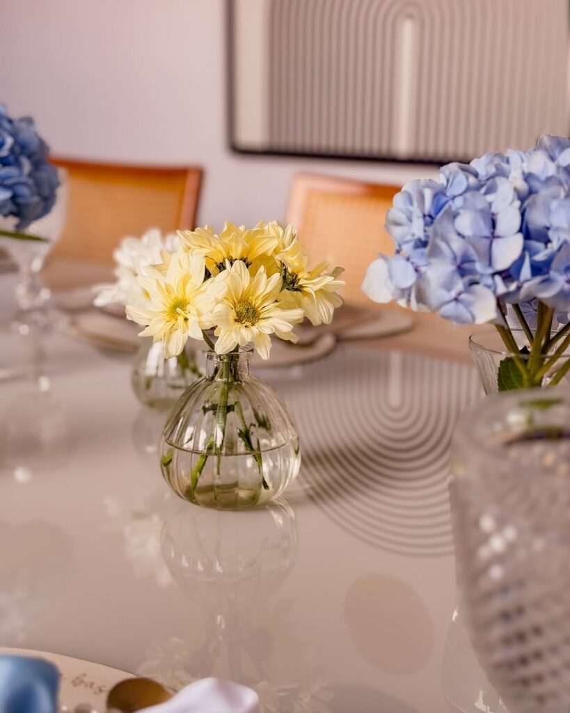 Mesa com vasinho de vidro transparente com flores do campo amarelas