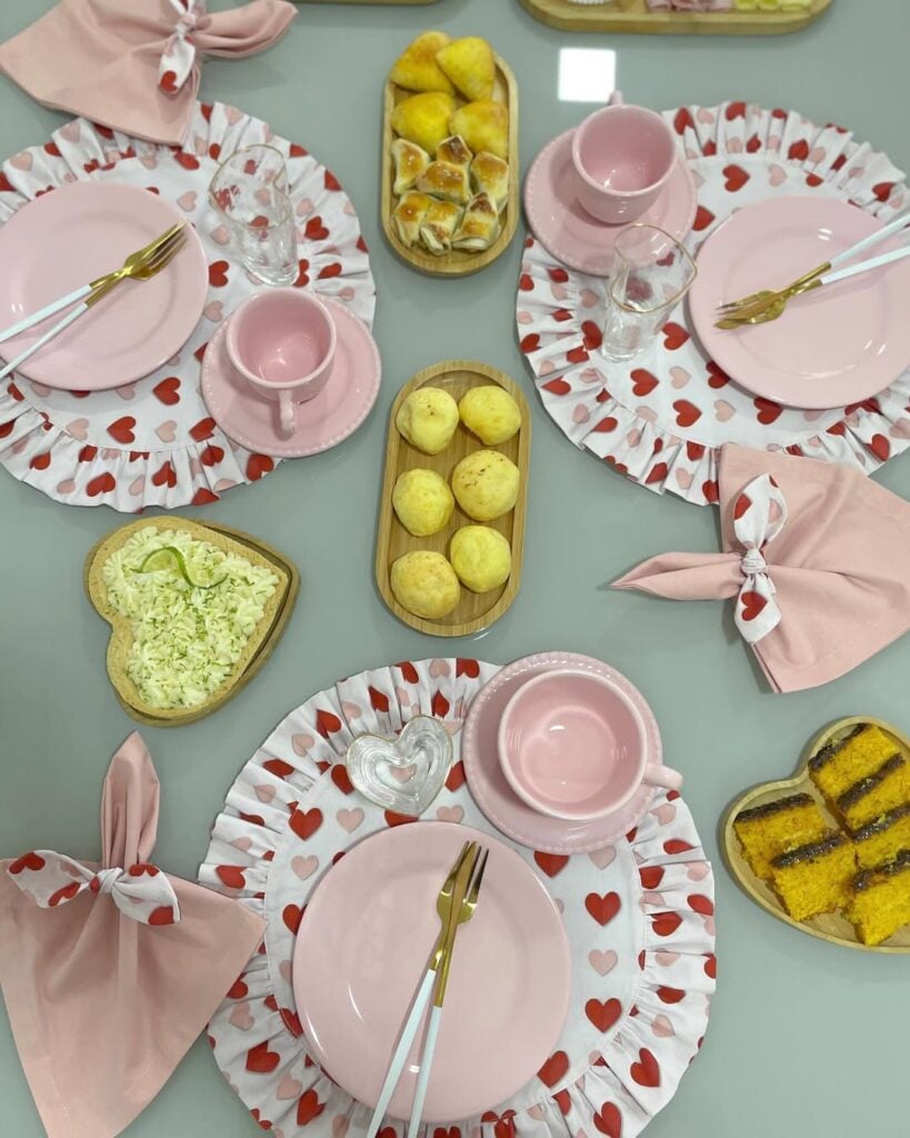 Mesa posta com sousplats brancos e corações vermelho e rosas e louça rosa