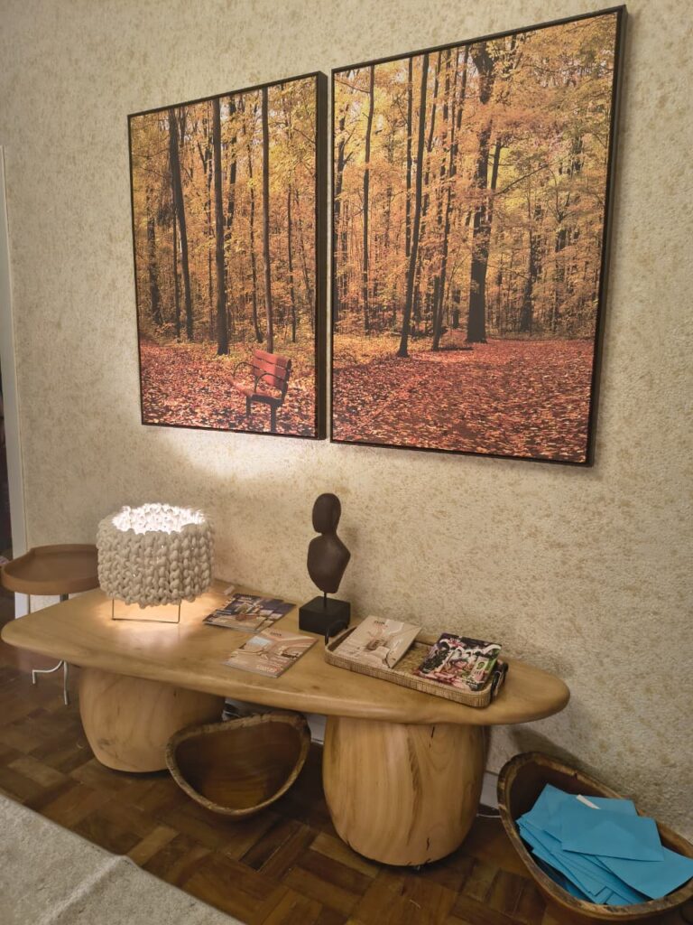 Espaço com quadros de paisagem outonoal, mesa de madeira orgânica e objetos decorativos