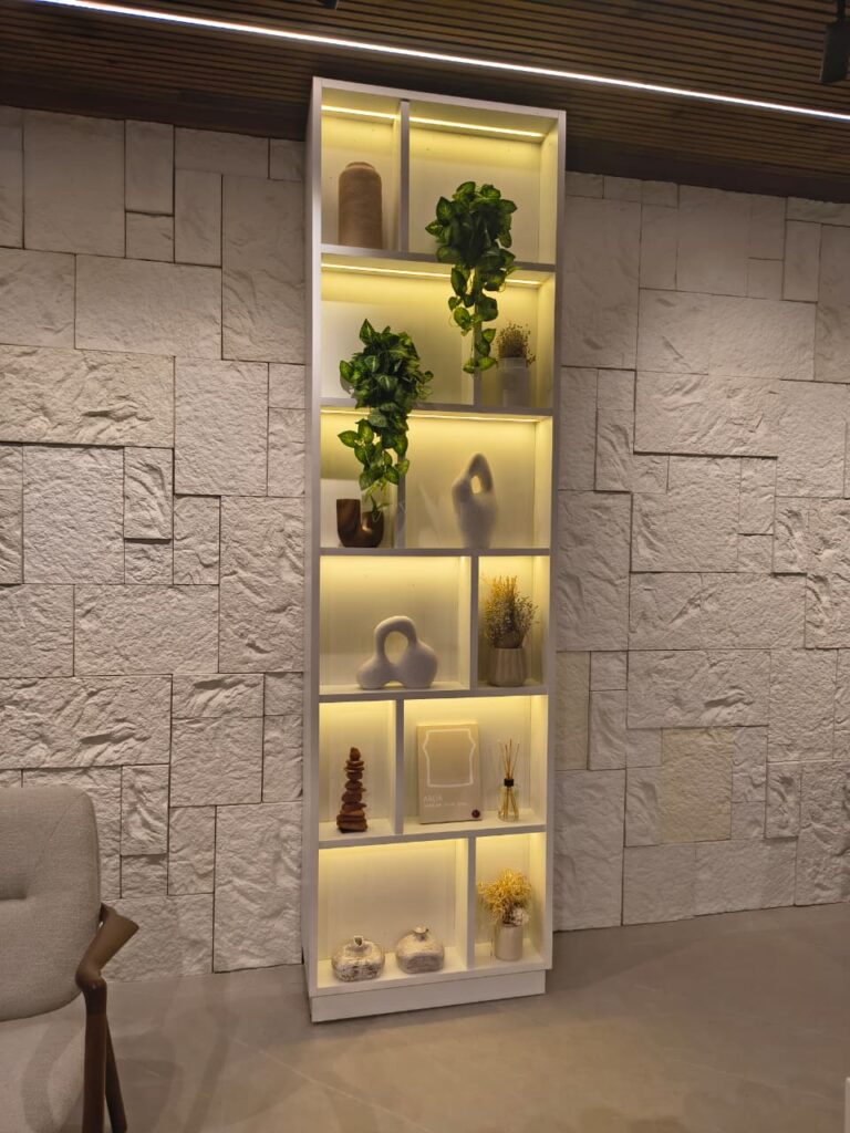 Estante branca com luz amarela, plantas e esculturas