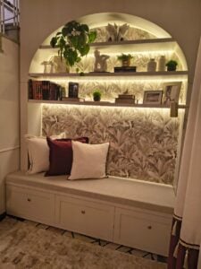 Cantinho com banco, almofadas, prateleiras, livros e objetos decorativos