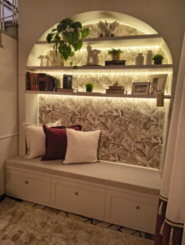 Cantinho com banco, almofadas, prateleiras, livros e objetos decorativos