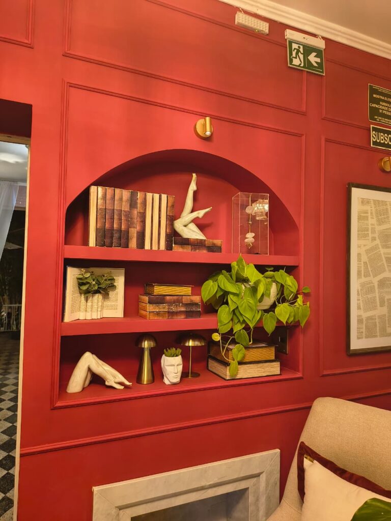 Estante vermelha com livros, planta e esculturas
