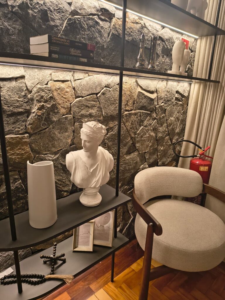 Parede de pedras, estante preta no estilo industrial com esculturas