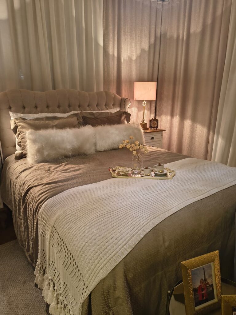 Quarto em tons de camurça e bege com cabeceira estofada em capitonê, bandeja e manta na cama