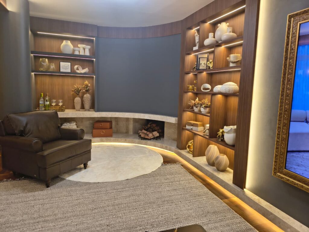 Sala de estar com poltrona marrom, estantes amadeiradas com cerâmicas e esculturas