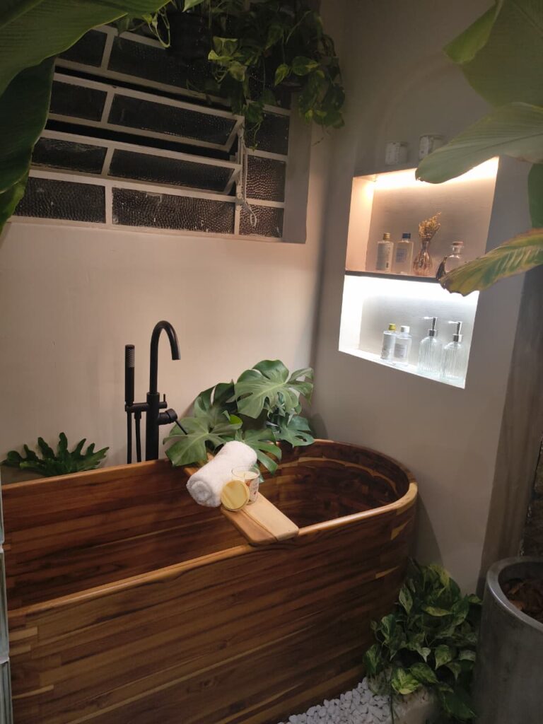 Banheiro com banheira de madeira, plantas, e nicho embutido com iluminação na parede