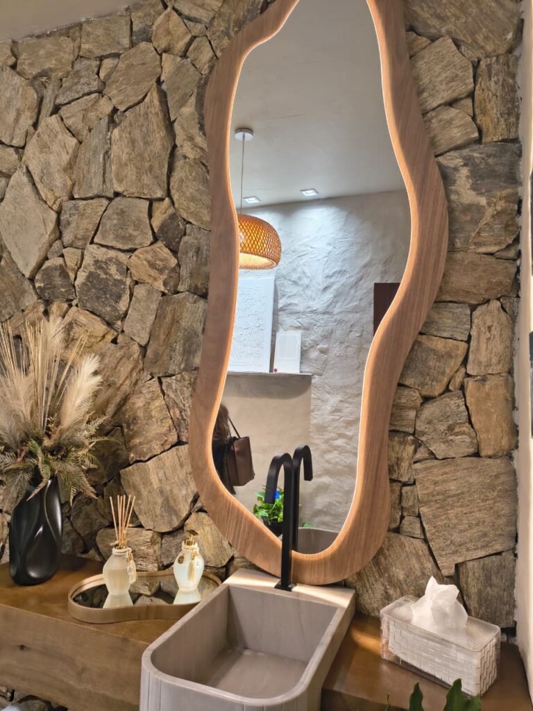 Banheiro com parede de pedras e espelho orgânico com LED
