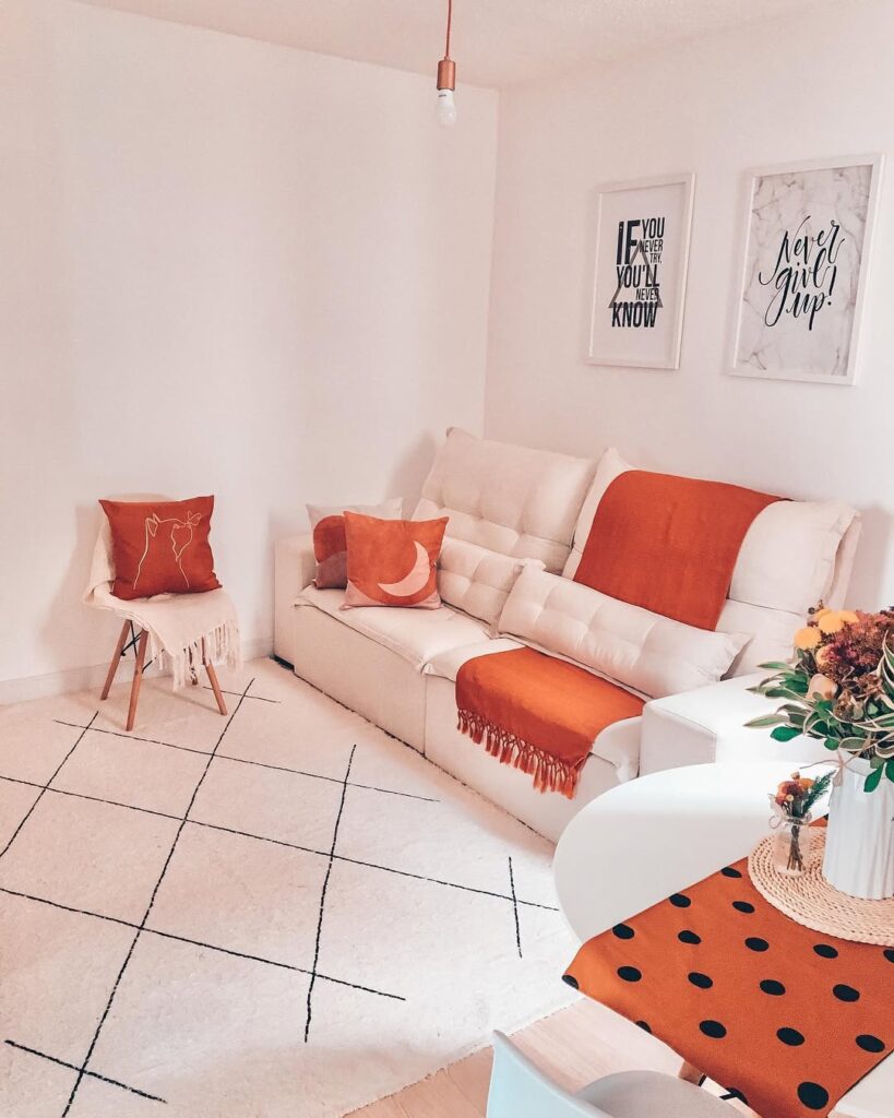 Sala de estar com paredes e sofá claro com manta e almofadas terracota
