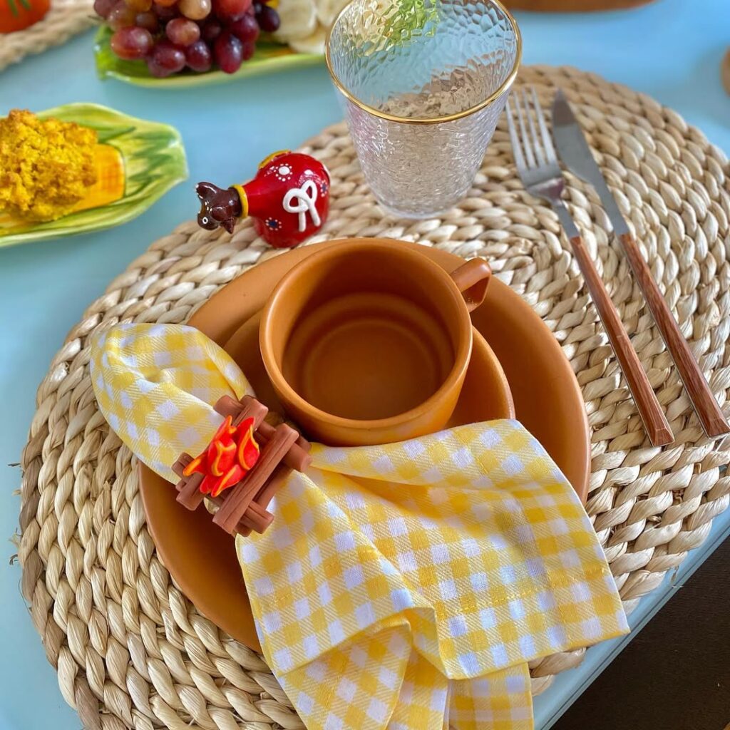 Mesa posta para café da manhã junino, com louça marrom, guardanapo xadrez em branco e amarelo e anel com mini fogueira