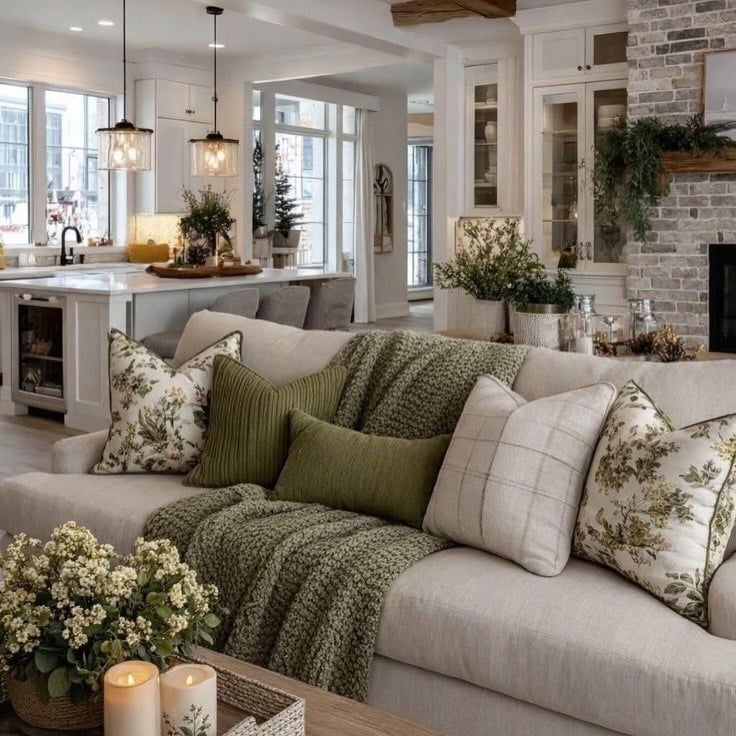 Sala com sofá claro, almofadas e manta verde, mesa de centro com flores e velas