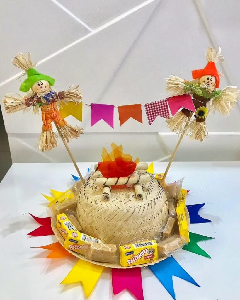 Centro de mesa junino com chapéu de palha decorado com espantalhos e bandeirinhas