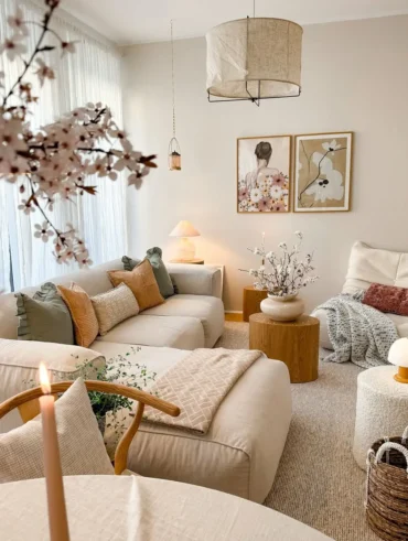 Sala de estar com paredes e sofás claros com mantas e almofadas, mesa de centro redonda e quadros na parede