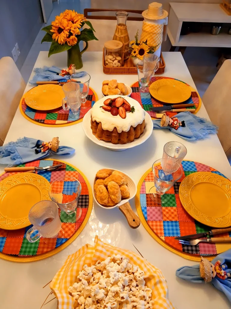 Mesa posta de São João com sousplats com xadrez coloridos, pratos amarelos e guardanapos azuis