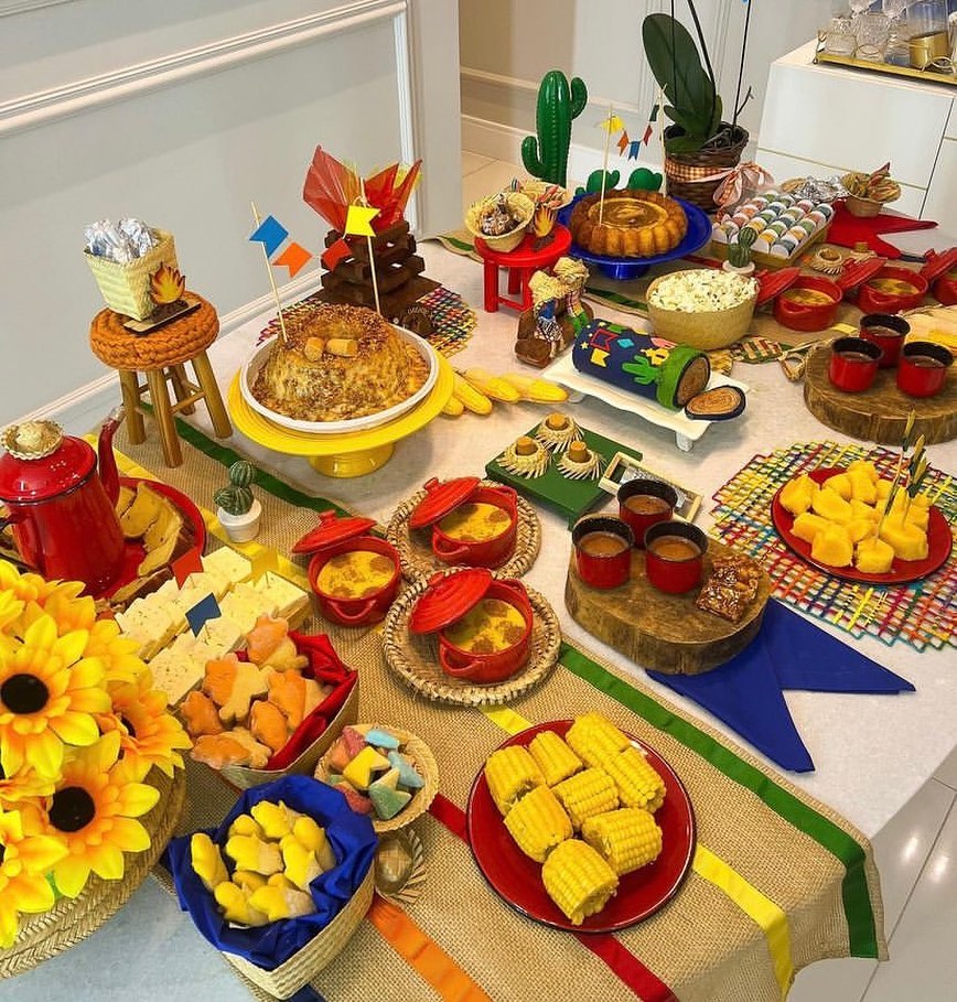 Mesa posta de São João com bandeirinhas, juta, sousplats xadrez, bolos, pipoca, milho