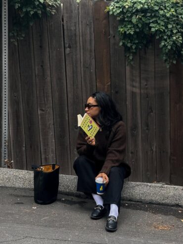 Mulher de cabelo escuro. Ela está sentada no chão com um livro
