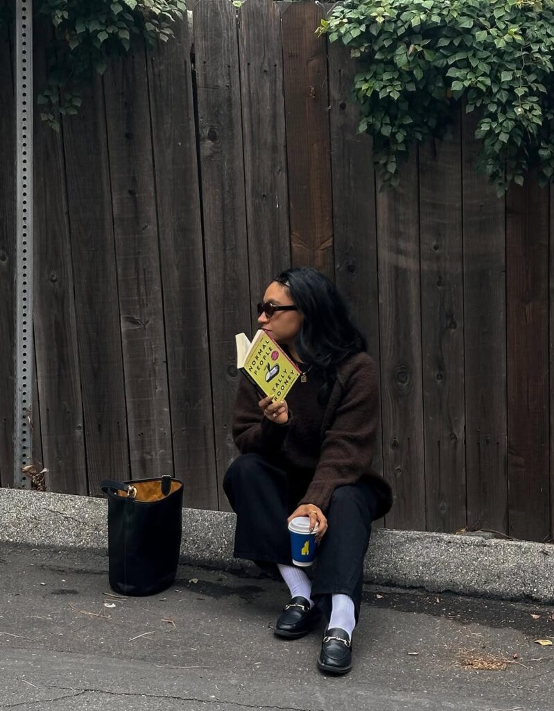 Mulher de cabelo escuro. Ela está sentada no chão com um livro
