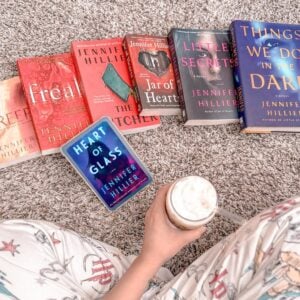 Pessoa sentada no chão, segurando um café gelado e livros na sua frente