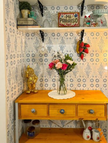 Cantinho com balcão de madeira, guardanapo de crochê e vaso de flores, azulejos com flores azuis e enfeites
