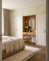 Quarto em cores neutras com guarda-roupa claro e penteadeira embutida em tons amadeirados