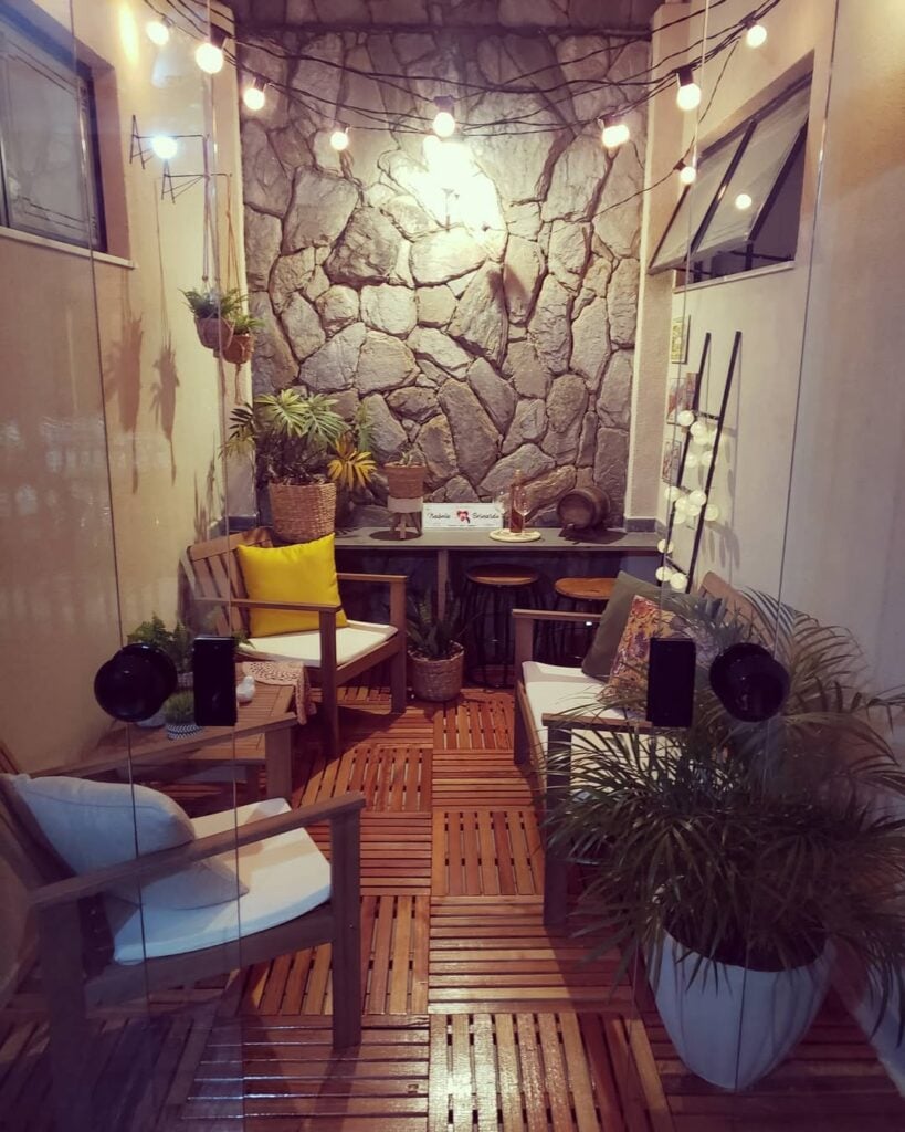 Jardim de inverno com parede de pedras, poltronas, banco e fio de lluzes
