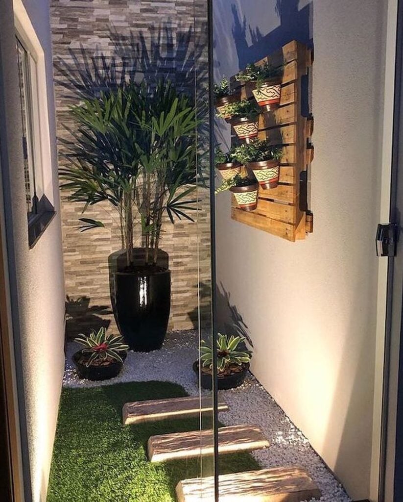 Jardim de inverno com vaso grande, pallet na parede com vasos pequenos e pedras brancas no chão
