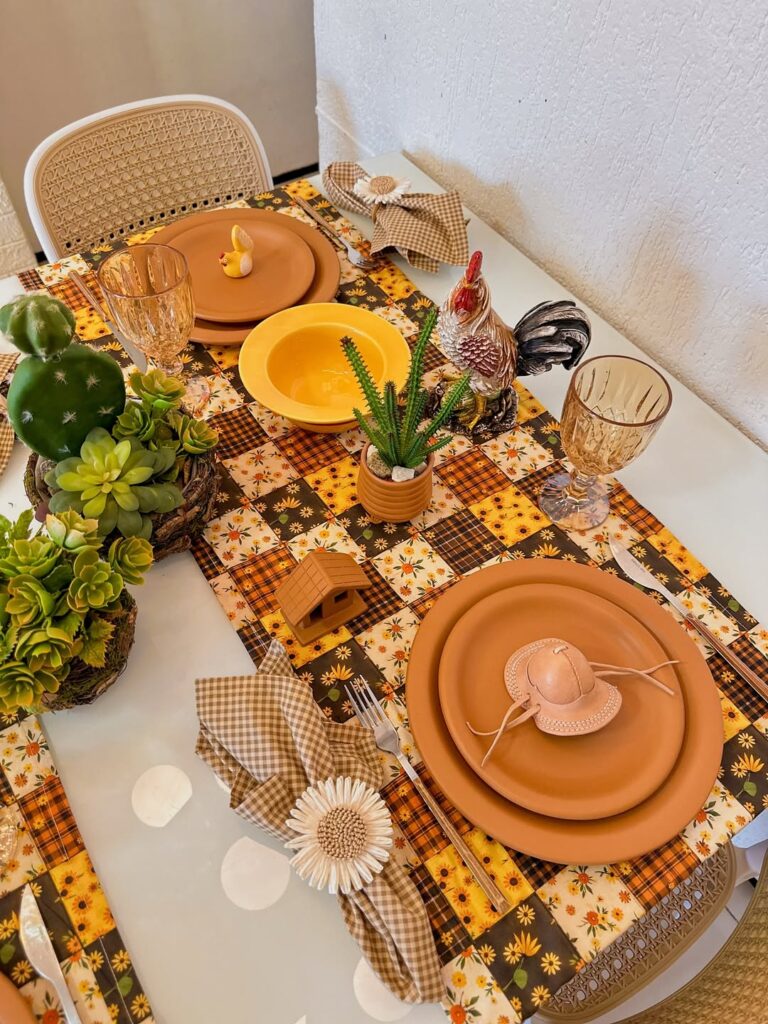 Mesa posta de São João com caminhos de mesa xadrez em tons de marrom e amarelo, louças marrom e enfeites como galo e casinha de madeira