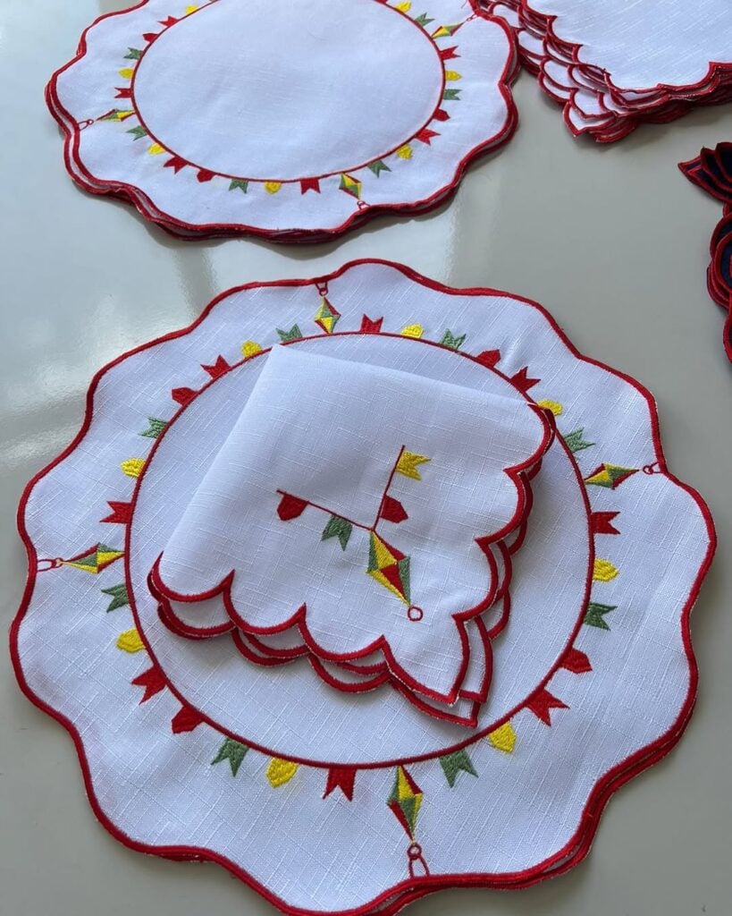 Jogo americano branco com borda vermelha e bandeirinhas coloridas bordadas