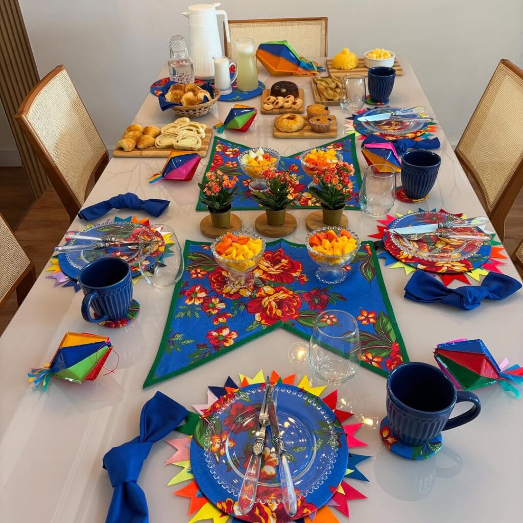 Mesa posta de café da manhã junino com sousplats azuis com bandeirinhas coloridas, louças e guardanapos azuis