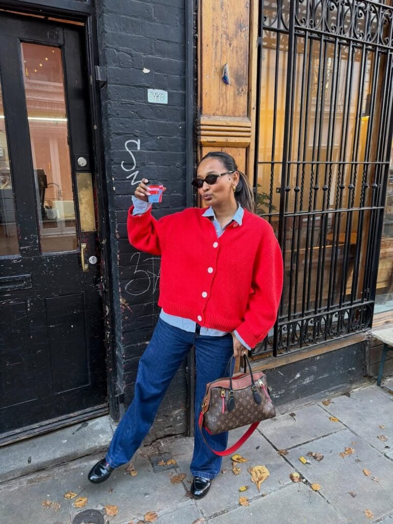 Mulher jovem e magra. Ela usa cardigan vermelho, camisa azul, calça azul-escuro e mocassim preto