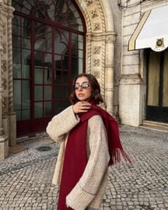 Mulher jovem de pele clara usando cachecol feminino vermelho e suéter marrom claro