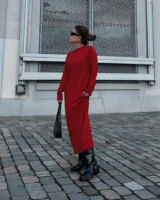 Mulher jovem, magra e de pele clara. Ela usa coque, vestido vermelho longo e bota biker preta