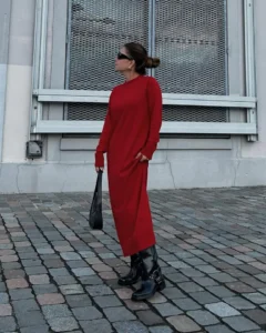 Mulher jovem, magra e de pele clara. Ela usa coque, vestido vermelho longo e bota biker preta