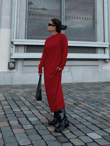 Mulher jovem, magra e de pele clara. Ela usa coque, vestido vermelho longo e bota biker preta