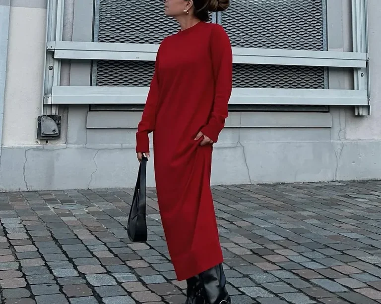 Mulher jovem, magra e de pele clara. Ela usa coque, vestido vermelho longo e bota biker preta