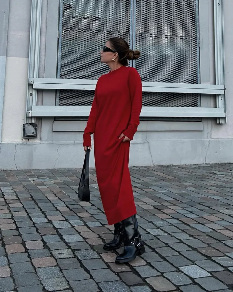 Mulher jovem, magra e de pele clara. Ela usa coque, vestido vermelho longo e bota biker preta