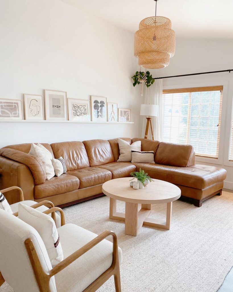 Sala com sofá caramelo em L, prateleira com quadros e tapete claro