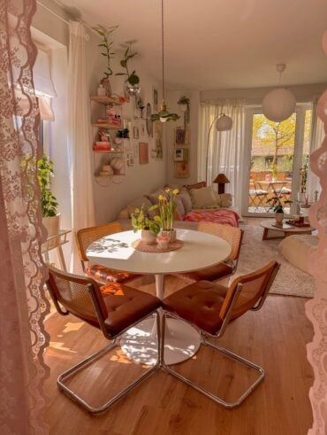 Sala de jantar e estar integradas com cortina de renda rosa, mesa redonda branca e cadeiras com assentos caramelos